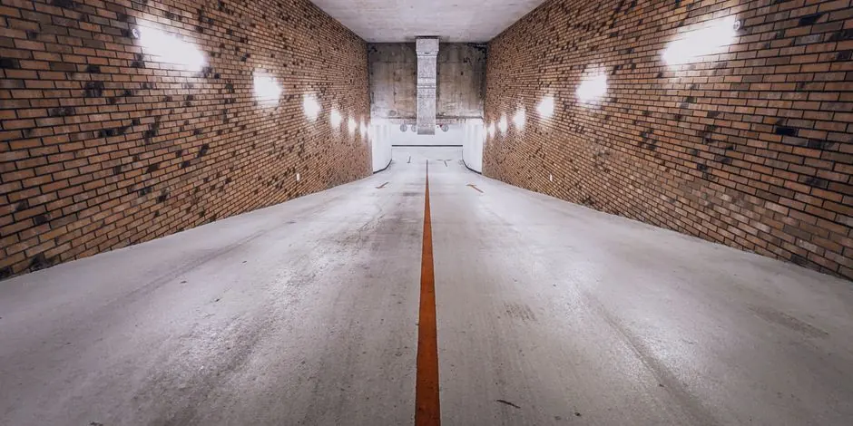 An underground brick-walled ramp with dim lighting and a single yellow line, creating a cinematic feel.