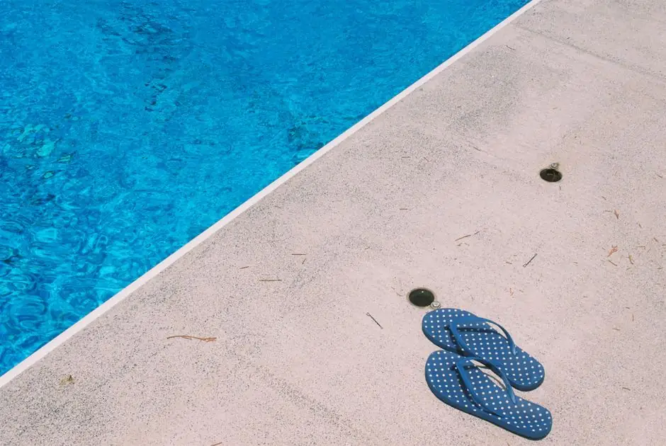 Blue polka dot slippers beside a clear swimming pool on a sunny day.