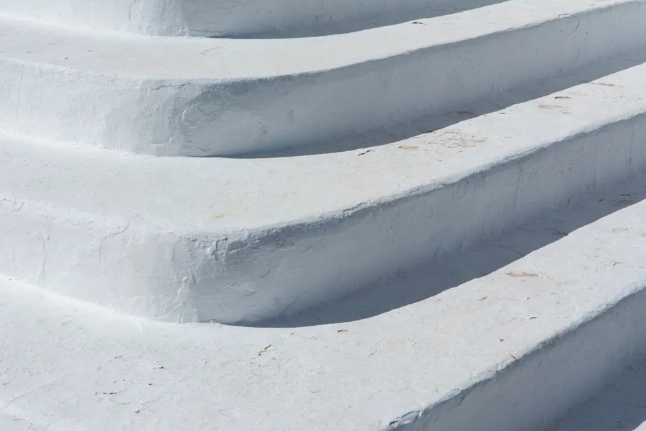 Close-up of textured white concrete steps in bright sunlight, showcasing minimalist design.
