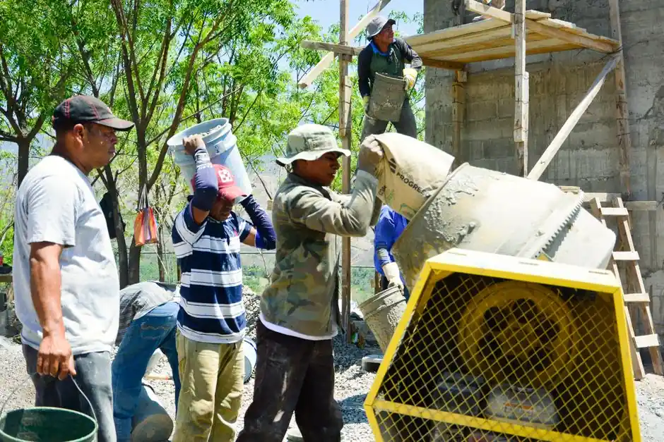 Outdoor construction site with workers pouring cement from mixers and buckets.