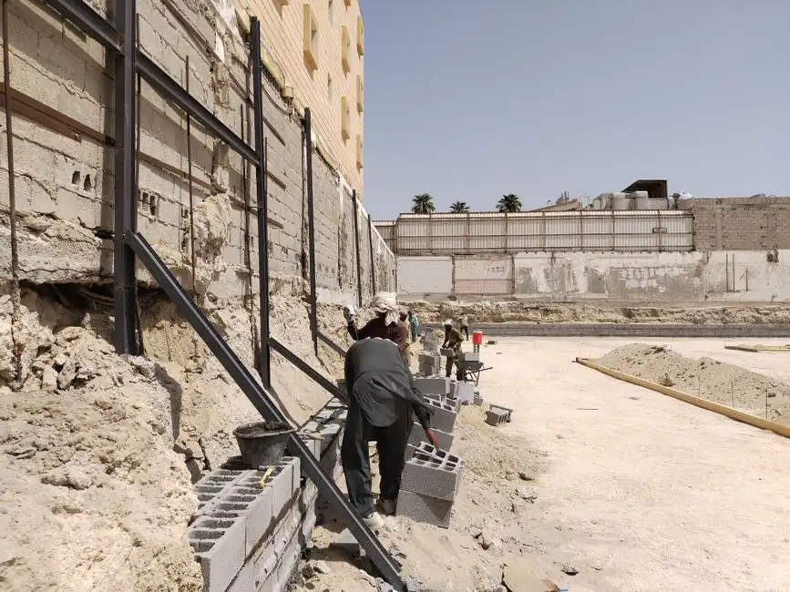 Workers building a concrete block retaining wall at a construction site under the clear sky.