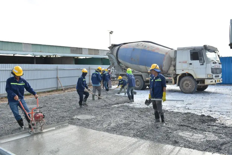Workers in safety gear pouring concrete outdoors with a cement mixer truck.